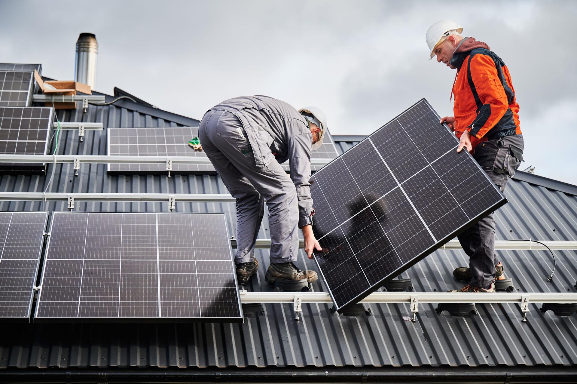 Technicians carrying photovoltaic solar module while installing solar panel system on roof of house